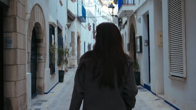A photograph from behind of a woman walking through the narrow streets of an old quarter somewhere in Spain. High quality 4k footage