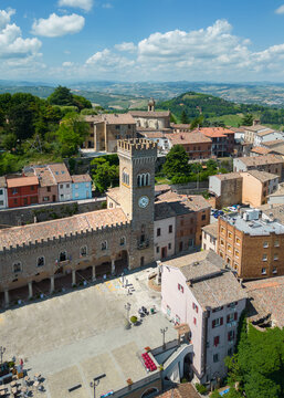 View of medieval architecture and a clock tower casting shadows on the cobblestone square, blending old-world charm with the vibrant hues of nature, Bertinoro, Italia.