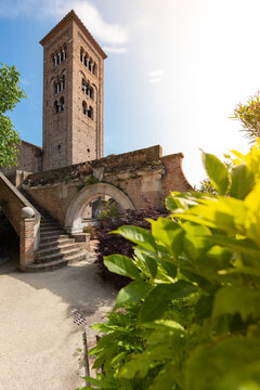 View of an ancient brick tower rises majestically above a stone arched bridge and lush greenery under a bright sky, Ravenna, Italia.