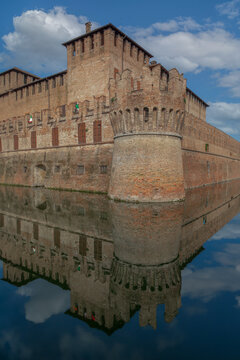 View of a formidable brick fortress mirrored in the tranquil moat under a serene sky, casting elongated reflections in Parma, Emilia Romagna, Italy.