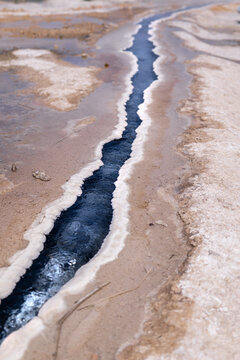 View of a narrow blue stream cutting through the pale, textured earth, creating a striking contrast of colors and textures, Annaba, Algeria.