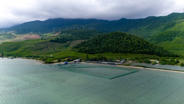 Aerial view of the tranquil lagoon embraces the oyster farm, framed by the lush green hills under a cloudy sky, tt. Lang Co, Hue, Vietnam.