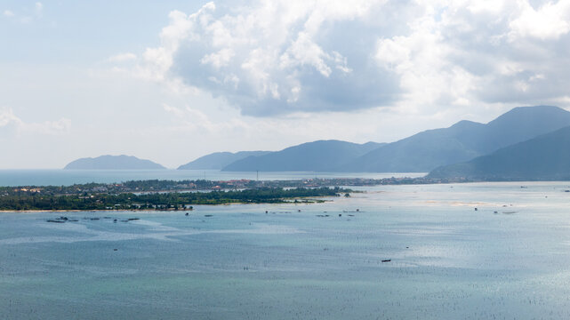 Aerial view of the oyster farm in the blue lagoon surrounded by green islands and distant mountains under a cloudy sky, tt. Lang Co, Hue, Vietnam.