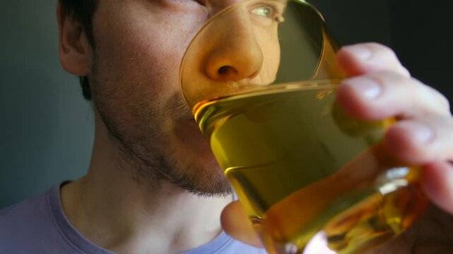 Close up young caucasian man drinking clean water from glass tumbler to quench thirst, showing importance of healthy lifestyle, proper daily hydration. Thirsty man drinking fresh pure water from glass