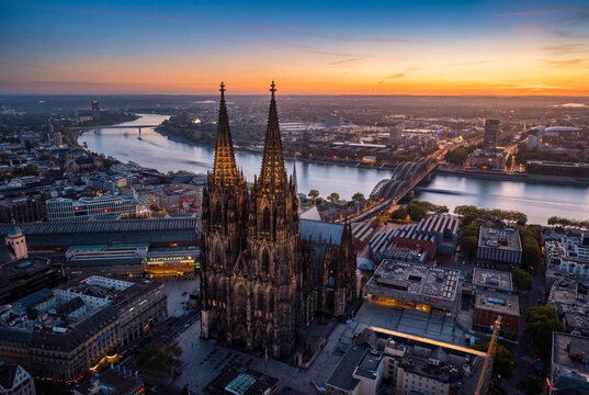 Aerial view of the magnificent Cologne Cathedral piercing the skyline as the Rhine River reflects the warm glow of the setting sun, Cologne, North Rhine-Westphalia, Germany.