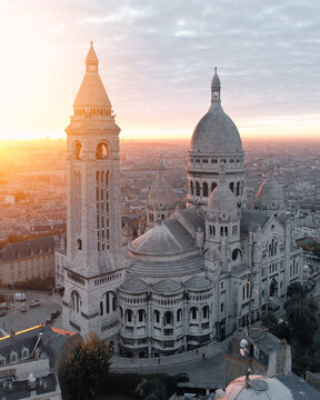 Aerial view of the Sacre-Coeur Basilica bathed in the warm glow of sunrise, its white stone contrasting against the soft hues of the Parisian dawn, Paris, France.