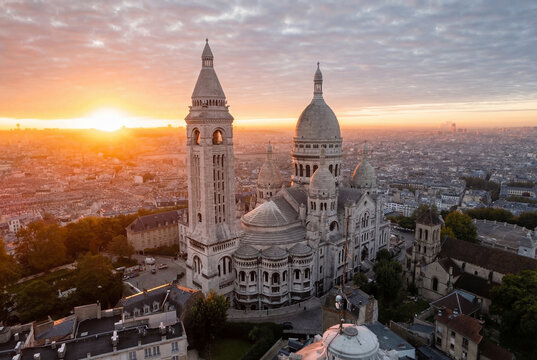 Aerial view of the Sacre-Coeur Basilica bathed in the warm glow of the sunrise, its white stone contrasting against the urban tapestry below, Paris, France.