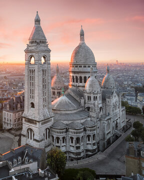 Aerial view of the Sacre-Coeur Basilica stands majestically against a soft, pastel sunrise, its white stone glowing warmly, Paris, France.
