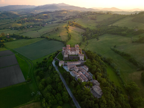 Aerial view of Torrechiara Castle perched atop a verdant hill, kissed by the golden hues of the setting sun, against the backdrop of rolling hills, Parma, Emilia Romagna, Italy.