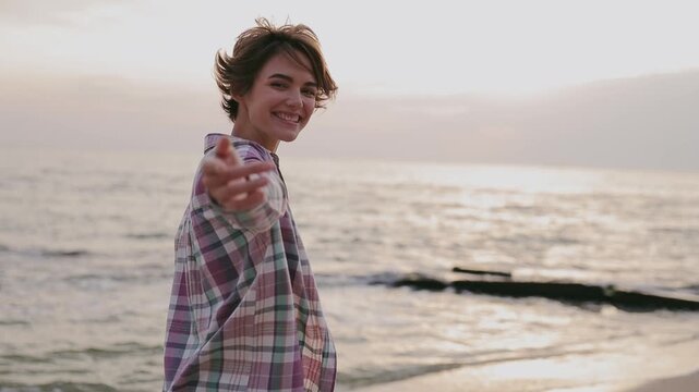 Young smiling happy fun woman wearing shirt casual clothes call somebody to follow her rest relax in free time go walk on sea ocean sand shore beach outdoor seaside in summer day. Lifestyle concept