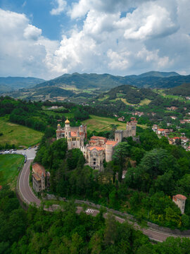 Aerial view of Rocchetta Mattei, a medieval castle with vibrant colors nestled among rolling hills and lush greenery, Bologna, Italy.