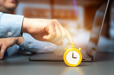 Businessman presses a stopwatch and an alarm clock while sitting in an office at a laptop. Concept of deadline pressure, time management, urgency, productivity, multitasking, and work efficiency