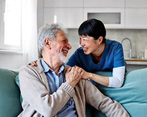 Doctor or nurse caregiver with senior man talking and having fun at home or nursing home