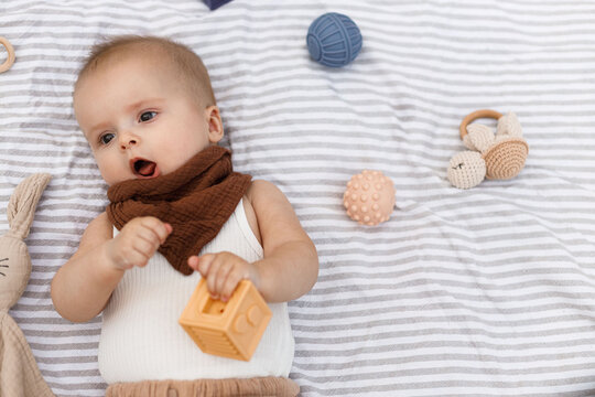 Beautiful happy baby lying on blanket with toys and teether in summer garden. Top view. Portrait of cute joyful baby relaxing in park, enjoying summer outdoors. Childhood