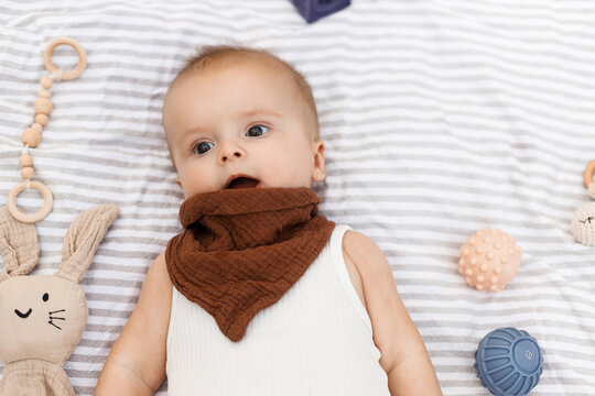 Beautiful happy baby lying on blanket with toys and teether in summer garden. Top view. Portrait of cute joyful baby relaxing in park, enjoying summer outdoors. Childhood