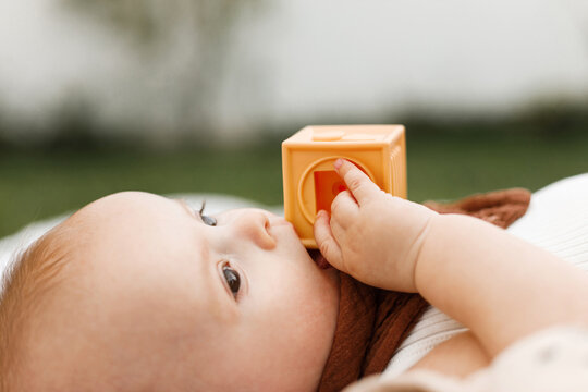 Beautiful happy baby lying on blanket and playing with toys on background of sunny summer garden. Childhood. Portrait of cute infant relaxing in park, enjoying summer outdoors