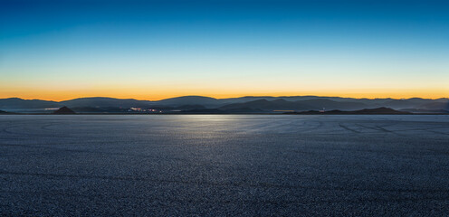 Obraz premium Vast empty asphalt pavement with mountain silhouettes under a clear blue hour sky