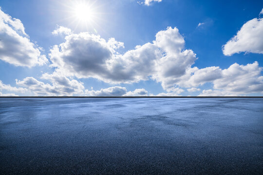 Empty asphalt pavement background under a bright sunny sky with clouds, ideal for car product placement.