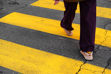 Fototapeta premium Person walks on yellow crosswalk lines in urban area on a clear day