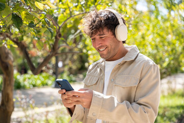 Fototapeta premium A man enjoys listening to music with headphones in a park while using his phone