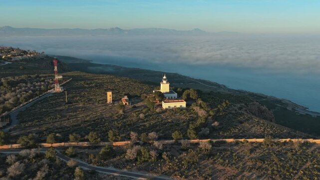 Aerial view tracking the santa pola lighthouse in spain, revealing a stunning sea of clouds covering the mediterranean at sunrise
