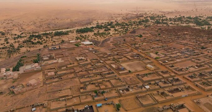 Desert Settlement Of Ouadane In Central Mauritania, With Earth-toned Buildings And Walled Courtyards On Sandy Landscape. aerial tilt-down shot