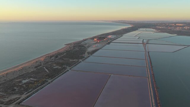 Golden hour aerial footage flying over the pink salt lakes of salinas de santa pola in spain, showing the coastline and salt evaporation ponds