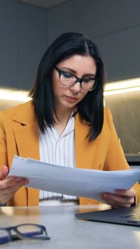 Remote work at home concept where charming confident hardworking successful female office manager in formal clothes sitting on cuisine background and working checking business documents using tablet