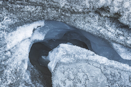 A stream with blue water flows through an icy canyon, carving its way through a perennial glacier and snowfield, and a mountain river flows through it. In the Tien Shan Mountains of the Pamirs