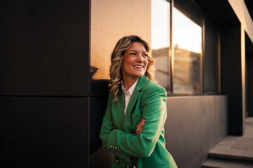 Fototapeta premium Confident businesswoman smiling leaning on urban building