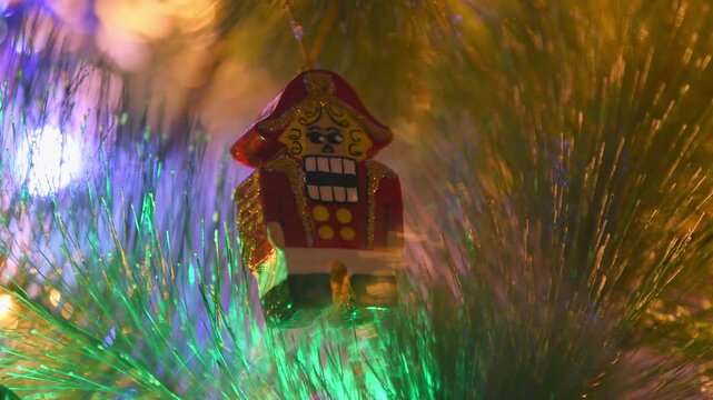 Colorful nutcracker ornament hanging on brightly lit christmas tree with glittering green tinsel