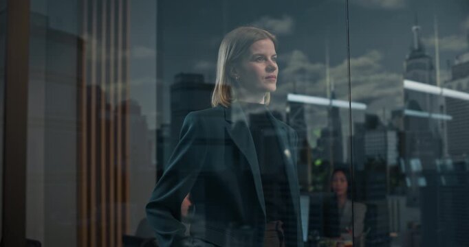 Young Caucasian Businesswoman Stands at a Floor-to-ceiling Office Window, Focused in Thought as City Skyscrapers seen in Reflection. Startup Finance, Strategy, Growth.