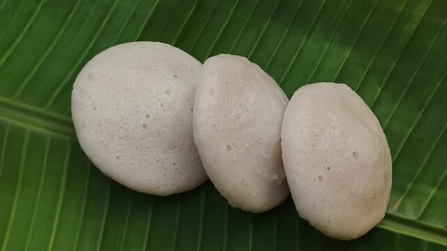 Homemade steamed rice cake, idali, iddali, idly or idli food served on banana leaf. Popular traditional south indian local vegan breakfast dish. Closeup rotating top view. Healthy kerala cuisine.