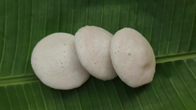 Closeup of hand serve healthy south indian breakfast dish steamed rice cake, idali, iddali, idly or idli food on banana leaf. Popular traditional homemade local vegan cuisine in india.