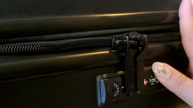 A macro shot of a black luggage suitcase showing the zipper detail and a built-in combination lock.