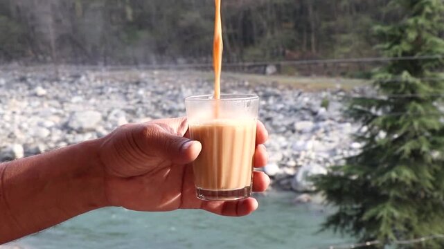 Tea getting pour in a transparent glass with a beautiful hilly background.