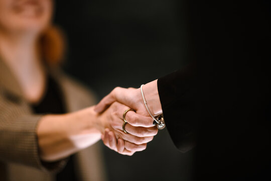Two people shaking hands in a professional setting during a business meeting at an indoor location with neutral colors in the background