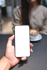 Vertical mockup image of a man holding mobile phone with blank screen with a blurred woman drinking coffee in background