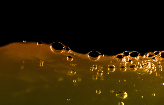 Golden orange liquid bubbles macro close-up with glossy surface, abstract oil or honey texture, vibrant yellow fluid background, high detail, smooth viscosity ideal for food, cosmetic science concepts