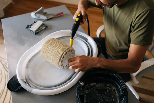 Top view of man cleaning humidifier filter using steam cleaner, removing dust and maintaining indoor air quality, thorough sanitizing technique