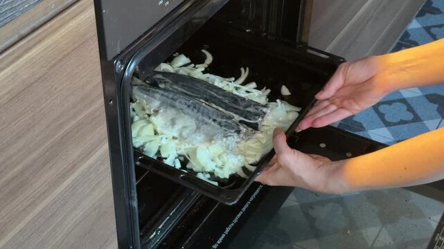 a girl puts fish in the oven to bake. mackerel with onions. dietary food. cooking baked fish.