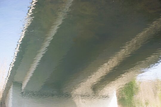 Abstraktes Motiv mit Spiegelung von Betonbr&uuml;cke auf Flusswasser mit kleinem Wellenmuster 