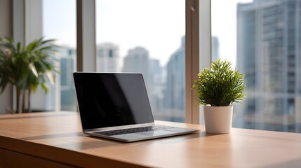 Obraz na płótnie Canvas A modern laptop and green plants on a wooden desk with a blurred city skyline view through a large window