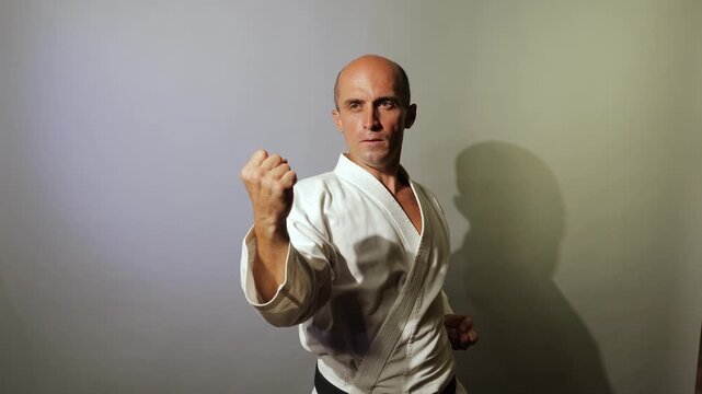 Against a light background, a young athlete with a black belt in a standing position makes blocks and strikes while moving