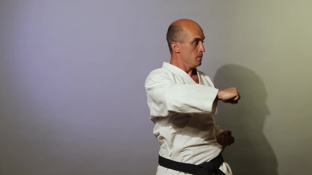 Against a light background, a young athlete with a black belt trains formal exercises