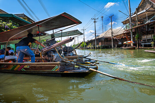 Auf dem Damnoen Saduk Floating Markt in Thailand rangiert ein Mann sein mit einem starken V8-Motor ausgestattet Ausflugsboot durch die engen Kan&auml;le; das Boot st&ouml;&szlig;t dunklen Rauch aus
