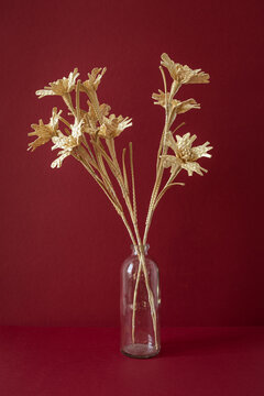 A glass vase with a bouquet of flowers made from straw on the red background. Straw weaving