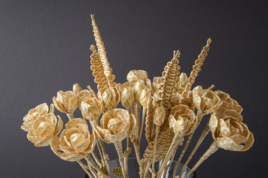 The bouquet flowers is made of straw on a gray background. Straw weaving. Small depth of field.