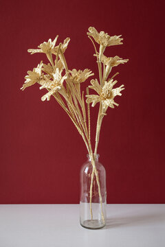 A glass vase with a bouquet of flowers made from straw on the red background. Straw weaving