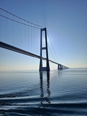 Fototapeta premium Wide view of suspension bridge over sea with clear sky and gentle waves, minimal coastal landscape
